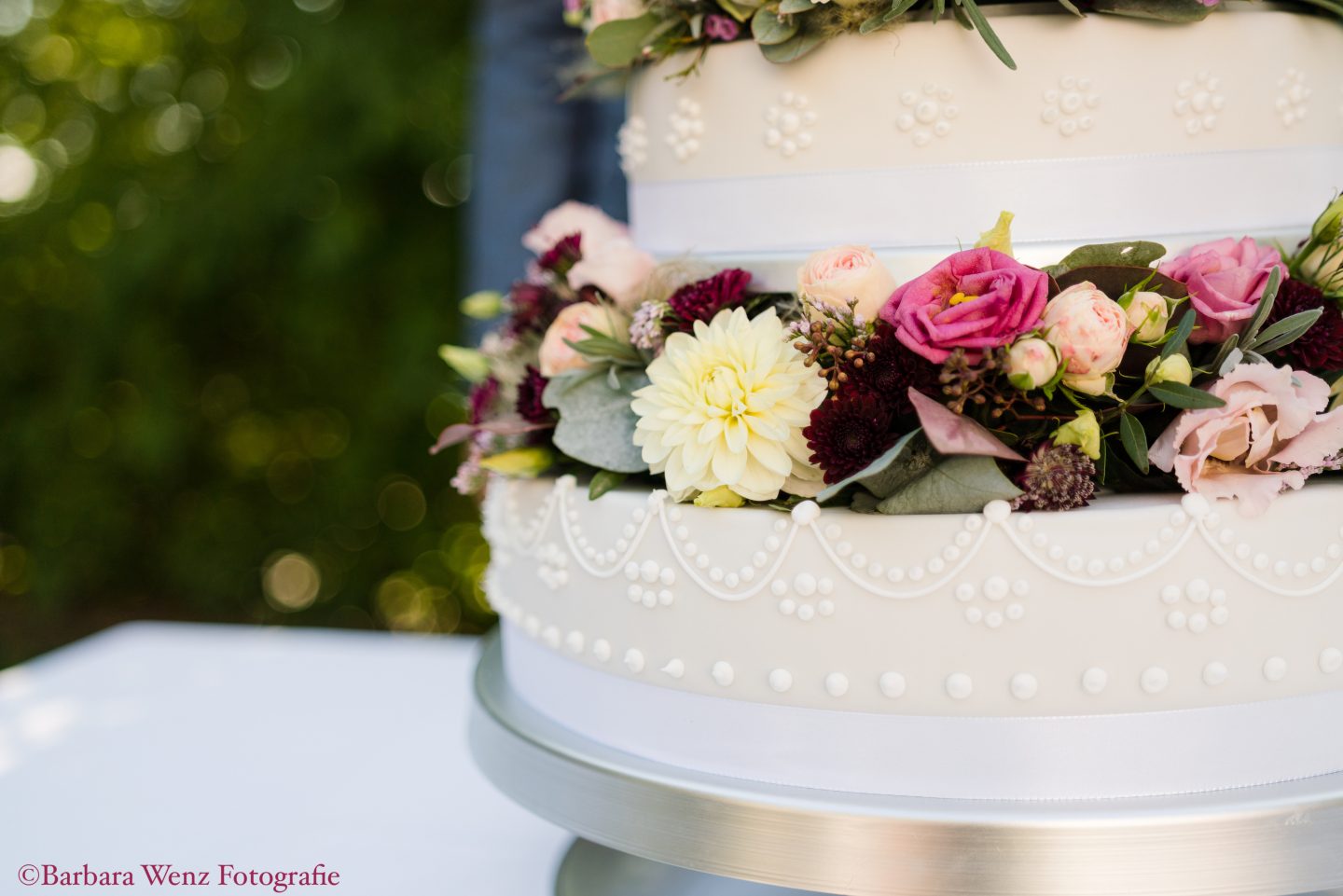 Großaufnahme einer weiß/cremefärbigen Hochzeitstorte, die mit echten Blumen in Creme- und Beeretönen geschmückt ist.