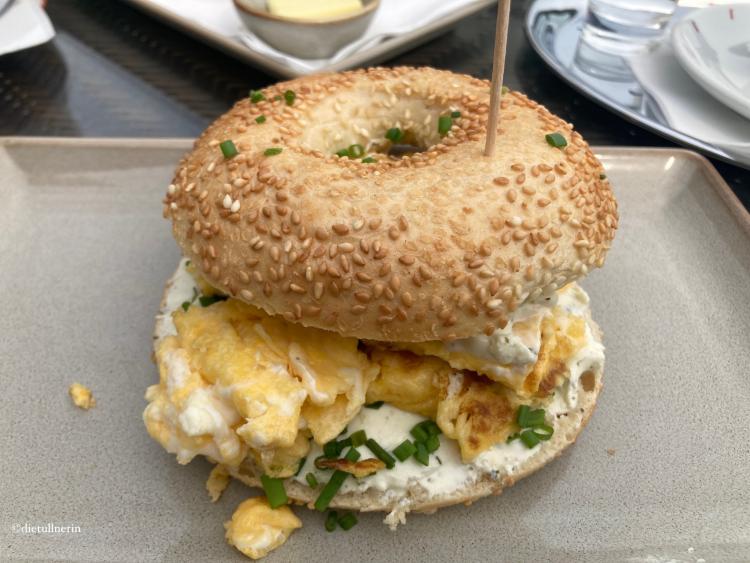 Bagel mit Eierspeis, Frischkäse und Schnittlauch auf eckigem, grauen Teller angerichtet.