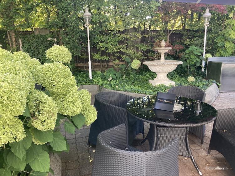 Romantisches Flair im Gartencafé dank Riesen-Hortensien, dunkler Korbmöbel, Brunnen und Laternen