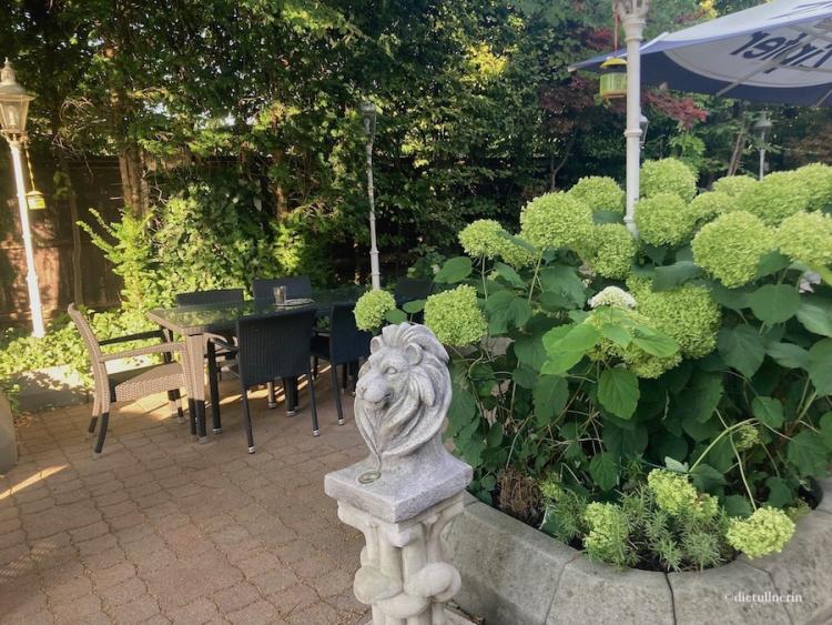 Löwenkopf-Statue vor imposanten Hortensien im romantischen Gartencafé